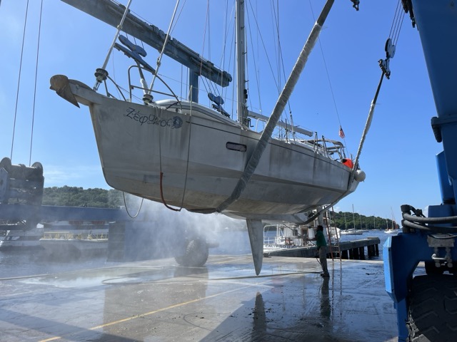 a sailboat in a lift, on slings and being pressure washed